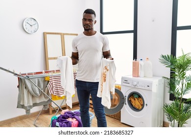 Young African Man Holding Clean White T Shirt And T Shirt With Dirty Stain Relaxed With Serious Expression On Face. Simple And Natural Looking At The Camera. 