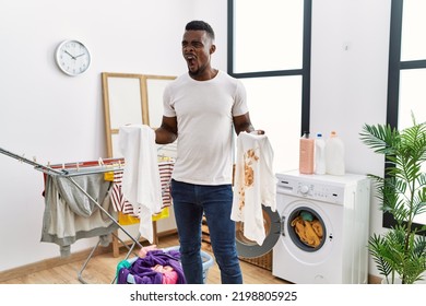 Young African Man Holding Clean White T Shirt And T Shirt With Dirty Stain Angry And Screaming Frustrated And Furious, Shouting With Anger. Rage And Aggressive Concept. 