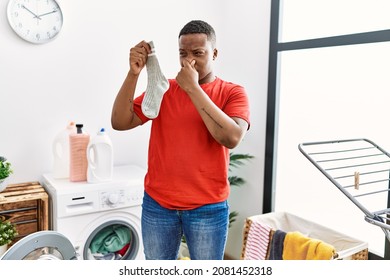 Young African Man Holding Dirty And Smelly Sock At Laundry Room