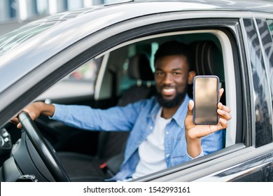 Young African Man Holding Phone With Screen While Sitting In His Car.