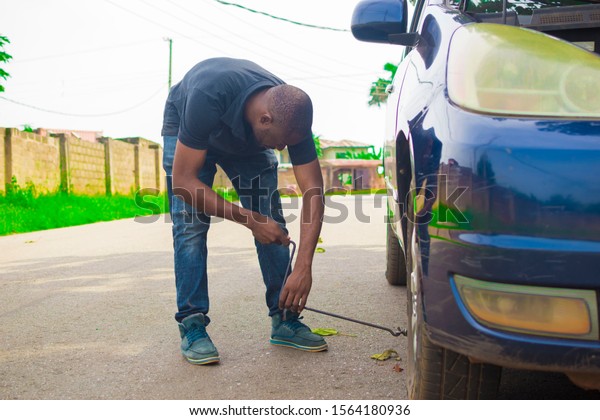 Young\
African man jacking up his car with a car\
jack