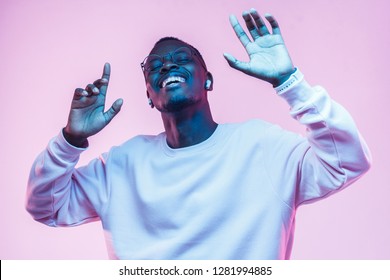 Young african man listening to music with wireless earphones and dancing isolated on pink background