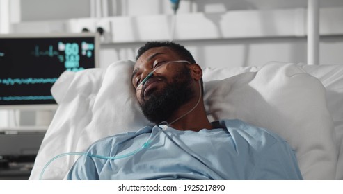 Young African Man Patient Suffering From High Fever Having Flu Or Cold While Lying With In Hospital Room. Afro-american Sick Man With Nasal Tube Sweating Lying In Hospital Bed