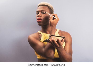 A Young African Man Posing On A Purple Background While Putting Makeup On His Face, Androgynous Concept.