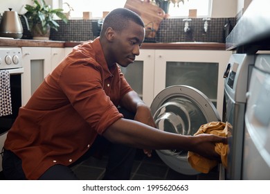 Young African man putting clothing into a washing machine at home - Powered by Shutterstock