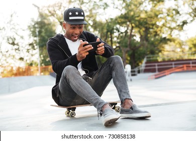 Young african man with a skateboard using smartphone while having rest in a skating zone - Powered by Shutterstock