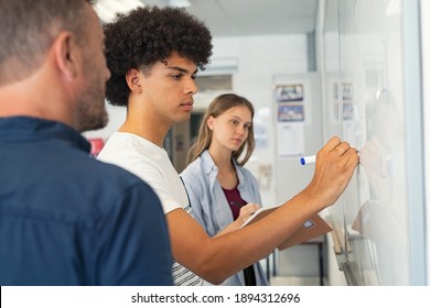 Young african man solving mathematics problem. College student solving algebra equation on white board in classroom. High school black guy trying to understand mathematics problem during lesson. - Shutterstock ID 1894312696