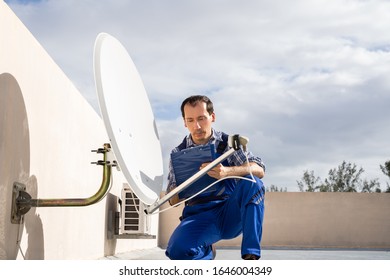 Young African Man In Uniform Fitting TV Satellite Dish On Roof - Powered by Shutterstock