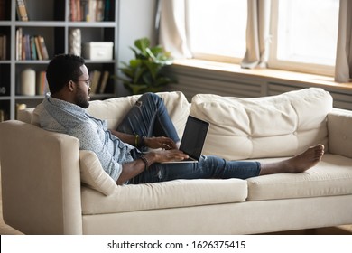 Young african man using laptop studying or working in app typing on computer lounge on sofa, millennial adult afro american male user holding notebook computer relax on couch in living room at home - Shutterstock ID 1626375415