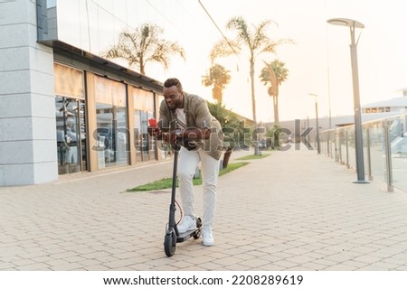 Young african man using a mobile phone on an electric scooter in the street during sunset
