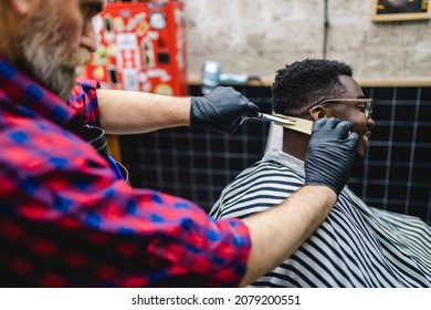 Young African man visiting hairstylist in barber shop. Professional hairdresser cut hair with scissors. 