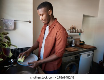 Young African man washing dishes in his kitchen at home - Powered by Shutterstock