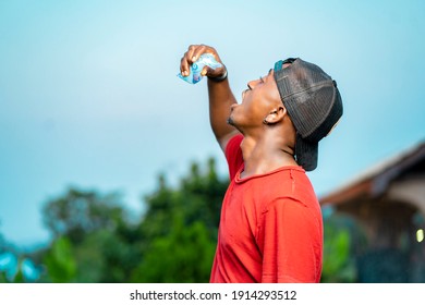 Young African Man Wearing Cap,  Sachet Of Water In Hand Dropping From Above Into His Mouth