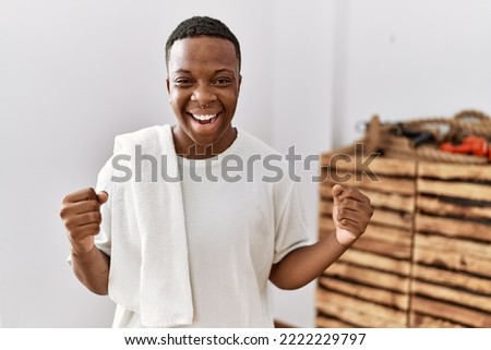 Young african man wearing sportswear and towel screaming proud, celebrating victory and success very excited with raised arms 