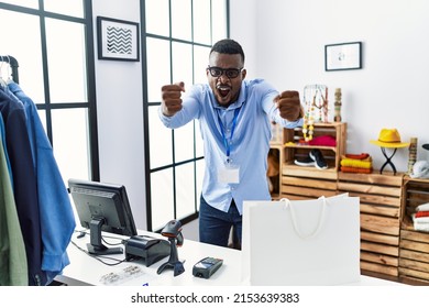 Young african man working as manager at retail boutique angry and mad raising fists frustrated and furious while shouting with anger. rage and aggressive concept. 
