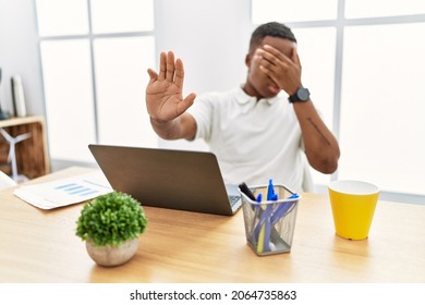 Young African Man Working At The Office Using Computer Laptop Covering Eyes With Hands And Doing Stop Gesture With Sad And Fear Expression. Embarrassed And Negative Concept. 