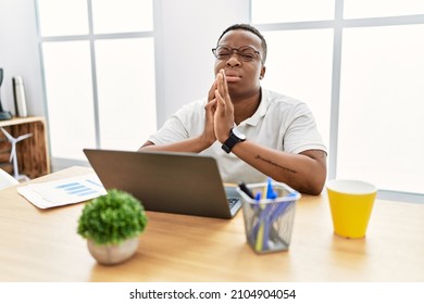 Young African Man Working At The Office Using Computer Laptop Begging And Praying With Hands Together With Hope Expression On Face Very Emotional And Worried. Begging. 