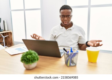 Young African Man Working At The Office Using Computer Laptop Clueless And Confused With Open Arms, No Idea Concept. 