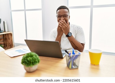 Young African Man Working At The Office Using Computer Laptop Laughing And Embarrassed Giggle Covering Mouth With Hands, Gossip And Scandal Concept 