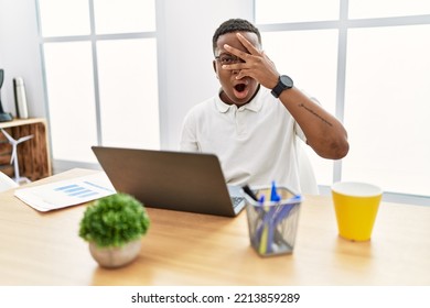 Young African Man Working At The Office Using Computer Laptop Peeking In Shock Covering Face And Eyes With Hand, Looking Through Fingers With Embarrassed Expression. 