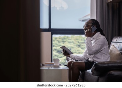 Young African Man Working Online from Home Using Tablet and Smartphone in Modern Living Room with Natural Light - Powered by Shutterstock