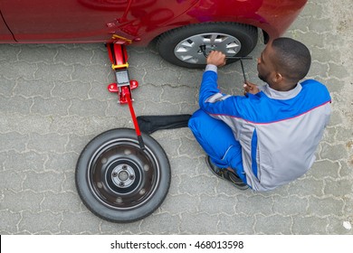 Young African Mechanic Changing Tire Of A Car With Wrench