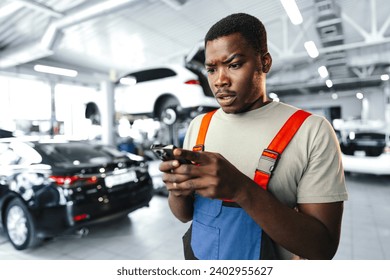 Young African mechanic man wearing uniform using mobile phone in a car service - Powered by Shutterstock