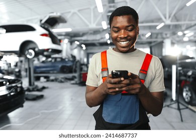 Young African mechanic man wearing uniform using mobile phone in a car service - Powered by Shutterstock