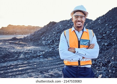 A young African mine worker wearing protective wear is looking at the camera with coal mine in the background - Shutterstock ID 2147533083