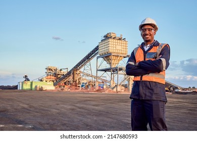 A young African mine worker wearing protective wear is looking at the camera with coal mine equipment in the background