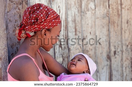 young african mother in the village holding her baby in front of the house