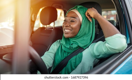 Young African Muslim Woman Driving A Car. Muslim Woman Driving Car, And Enjoys It. Smiling Black Muslim Woman Driving Her Vehicle And Drinking Coffee To Go. Arab Women Driving Car