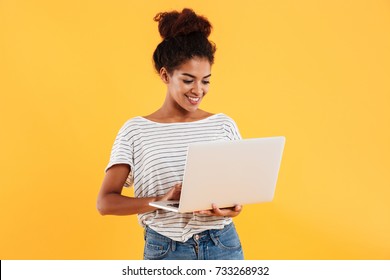 Young African Positive Cool Lady With Curly Hair Using Laptop And Smiling Isolated Over Yellow