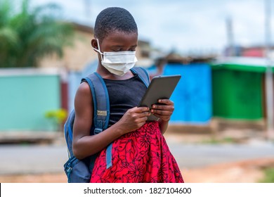 A Young African School Girl Wearing Bag Pack And Face Mask For Protection - Using Digital Tablet-concept On Child Education In Covid-19 Pandemic