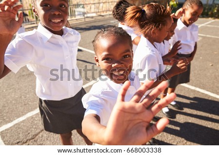 Young African schoolgirls in a playground waving to camera