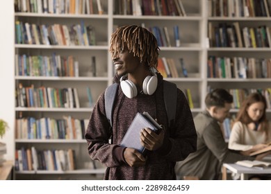 Young African student guy pose in library with schoolmates on background, smile look aside feels motivated gain new knowledge, enjoy excellent studies, wait for classes start. Studentship, education - Powered by Shutterstock