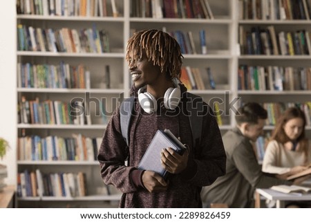 Young African student guy pose in library with schoolmates on background, smile look aside feels motivated gain new knowledge, enjoy excellent studies, wait for classes start. Studentship, education
