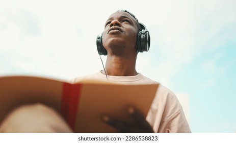 Young african student sitting outside of university and taking notes while study online with headphones - Powered by Shutterstock