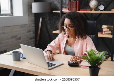 Young african student worker businesswoman freelancer counting funds domestic bills on calculator while using laptop for e-banking, paperwork, debt and loan