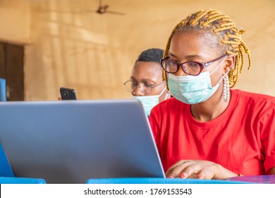 young african students in a classroom, one using a laptop, both wearing face masks