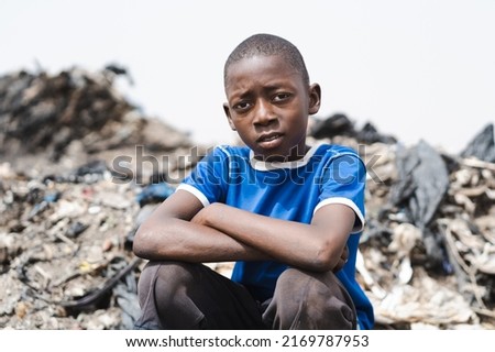 Young african waste collector sitting tired on top of a pile of plastic trash in a landfill contemplating the ugly surroundings; concept of poverty, child exploitation and human inequality