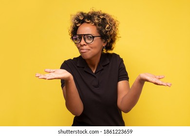 Young african woman with arms out, shrugging her shoulders, saying who cares, so what now. Studio shot on yellow wall. - Shutterstock ID 1861223659