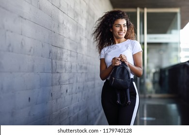 Young African woman with black curly hairstyle walking near business building. Happy Arab girl in sport clothes in the street.