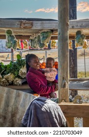 Young African Woman With Braids Holding A Child Selling Veggies And Fruit On The Street