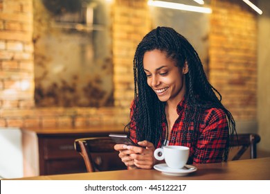 Young african woman at cafe drinking coffee and using mobile phone
 - Powered by Shutterstock