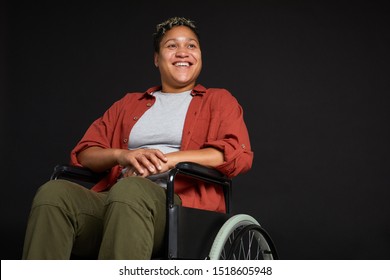 Young African woman with disabilities sitting in wheelchair and smiling isolated on black background
