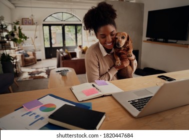 Young african woman embracing pet dog while working on laptop at home - Powered by Shutterstock