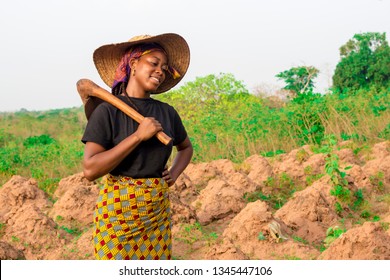 Young African Woman Farmer On A Farm Feeling Tired Holding A Hoe