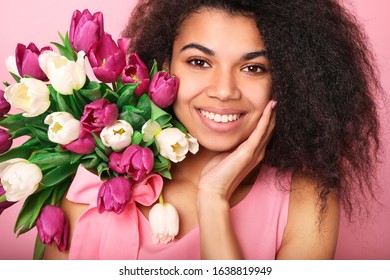 Young african woman with flowers on pink background. Women's day concept