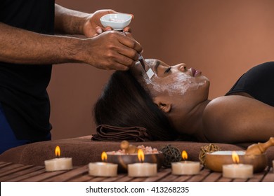 Young African Woman Getting Facial Mask At Spa